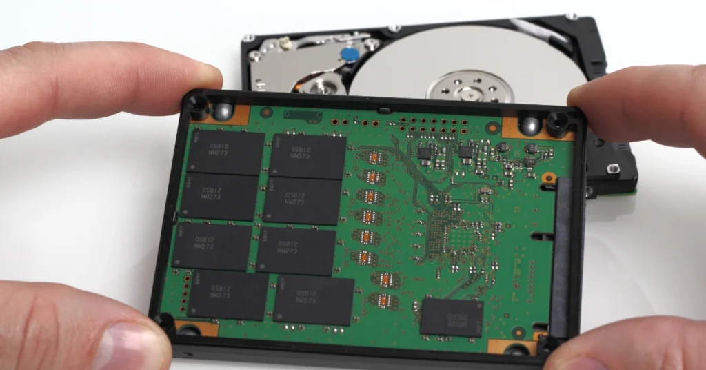 Close-up comparison of an SSD circuit board held next to an open HDD with visible platter.